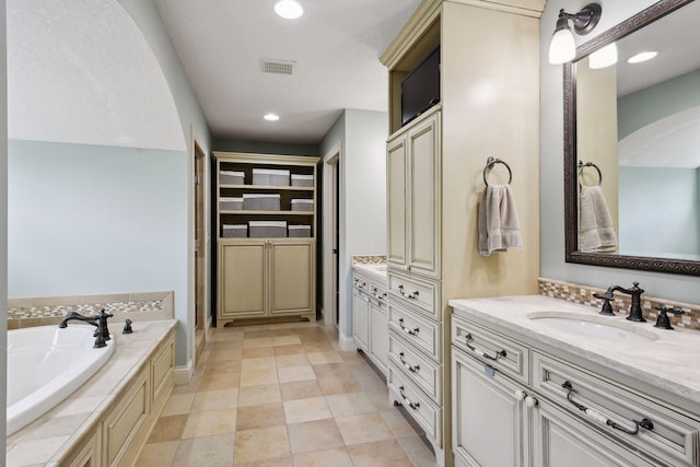 bathroom featuring tile patterned flooring, vanity, and tiled bath