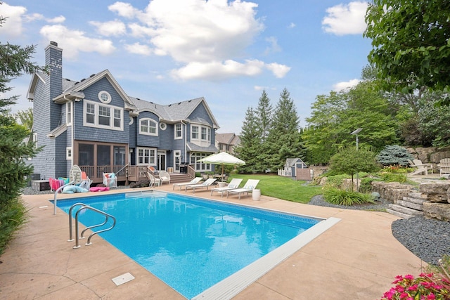 view of pool with a sunroom, a patio area, a deck, and a storage shed