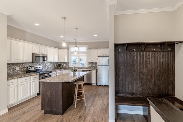 kitchen featuring white cabinetry, hanging light fixtures, stainless steel appliances, a kitchen island, and light wood-type flooring