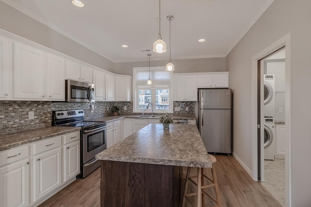 kitchen with a center island, sink, stacked washing maching and dryer, white cabinetry, and stainless steel appliances