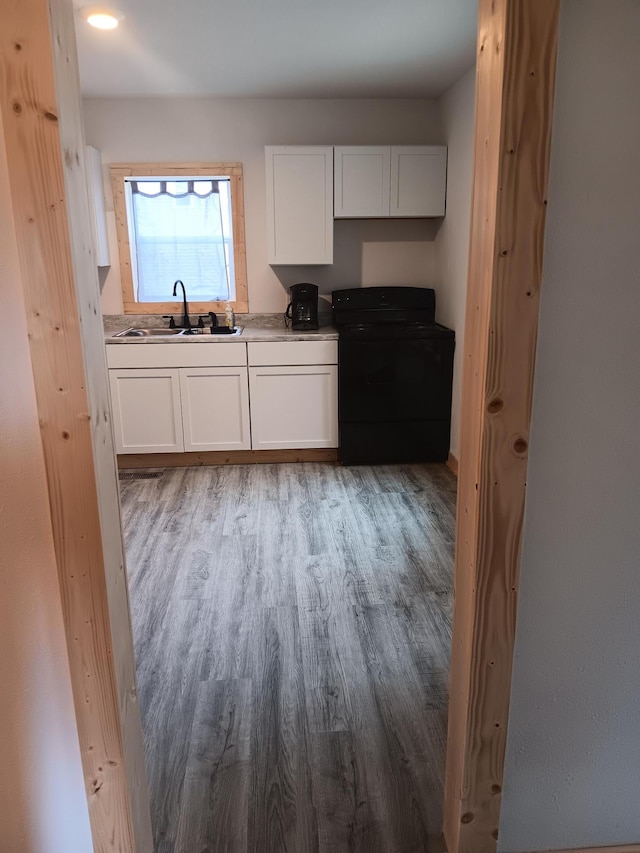 kitchen featuring white cabinetry, black electric range oven, light hardwood / wood-style floors, and sink