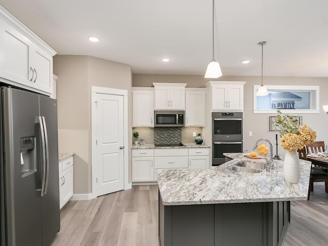 kitchen with a kitchen island with sink, hanging light fixtures, sink, appliances with stainless steel finishes, and white cabinetry