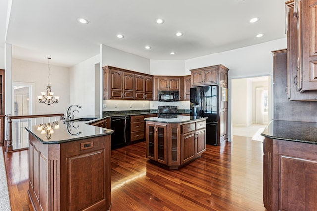 kitchen with sink, an inviting chandelier, hanging light fixtures, a center island with sink, and black appliances