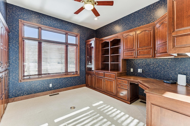 unfurnished office with ceiling fan, built in desk, and light carpet