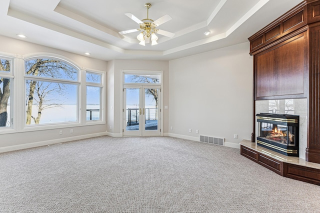 unfurnished living room featuring a tray ceiling, visible vents, a premium fireplace, carpet flooring, and baseboards