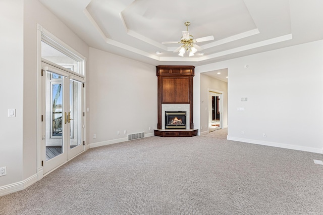 unfurnished living room with light colored carpet, a fireplace, visible vents, baseboards, and a tray ceiling