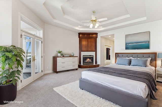 bedroom featuring baseboards, light colored carpet, access to exterior, a tray ceiling, and a fireplace