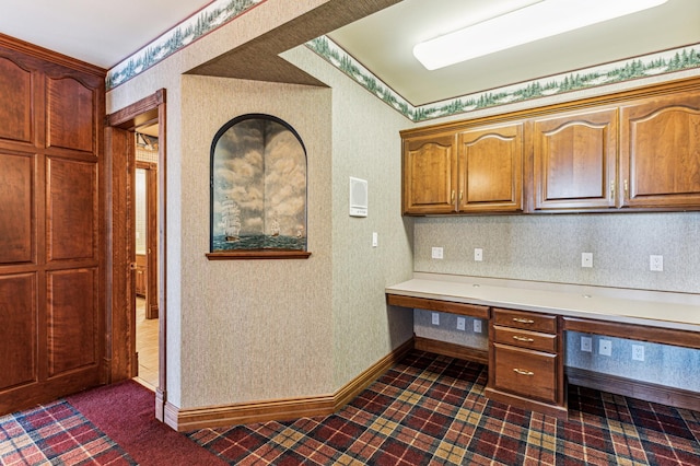 kitchen with brown cabinets, built in desk, light countertops, baseboards, and wallpapered walls