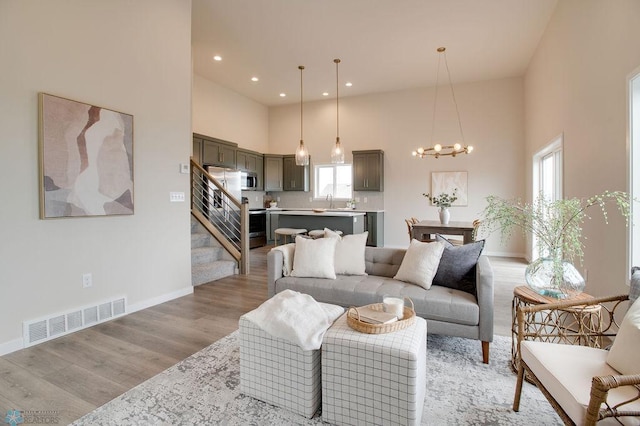 living room featuring an inviting chandelier, a towering ceiling, sink, and light hardwood / wood-style flooring