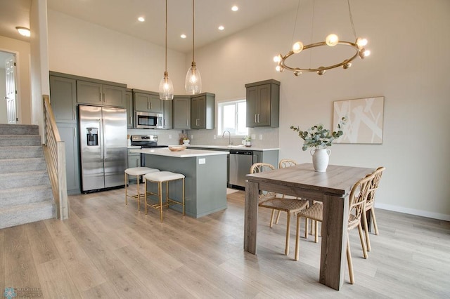 kitchen with a center island, hanging light fixtures, a towering ceiling, decorative backsplash, and appliances with stainless steel finishes