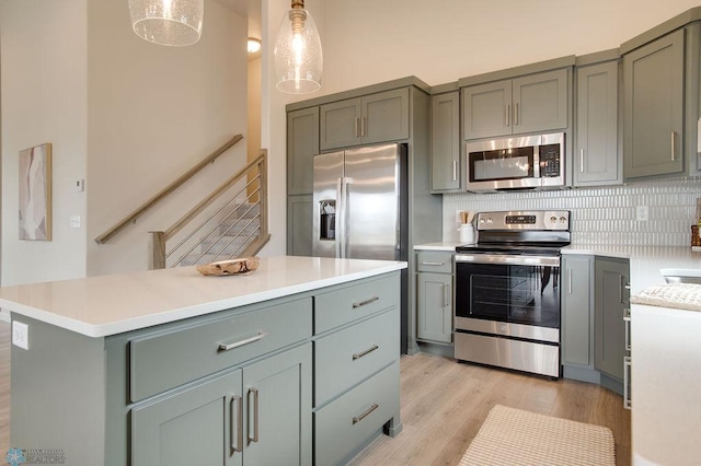 kitchen with appliances with stainless steel finishes, backsplash, decorative light fixtures, light hardwood / wood-style flooring, and a kitchen island