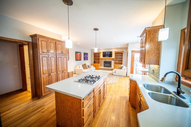 kitchen featuring sink, a center island, light hardwood / wood-style flooring, stainless steel gas stovetop, and a fireplace