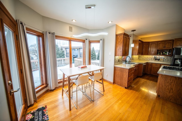 kitchen featuring black fridge with ice dispenser, sink, light hardwood / wood-style flooring, pendant lighting, and backsplash