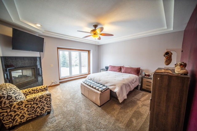 carpeted bedroom featuring ceiling fan, a fireplace, and a raised ceiling