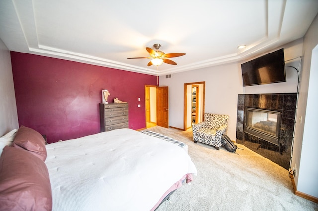 carpeted bedroom with ceiling fan, a tiled fireplace, and a raised ceiling