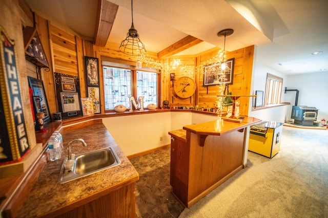 kitchen with sink, dark colored carpet, decorative light fixtures, an island with sink, and beamed ceiling