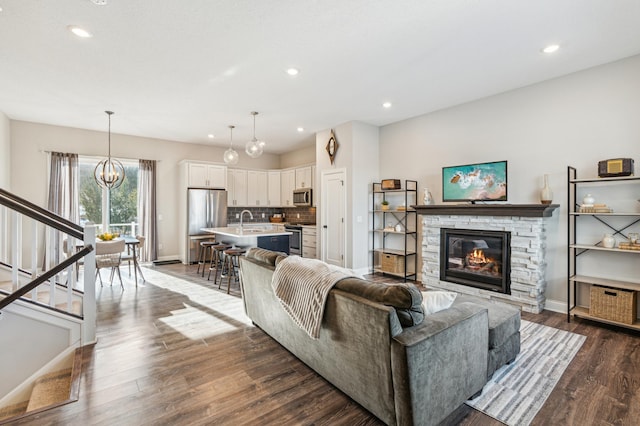 living room featuring dark hardwood / wood-style flooring, sink, a stone fireplace, and a chandelier