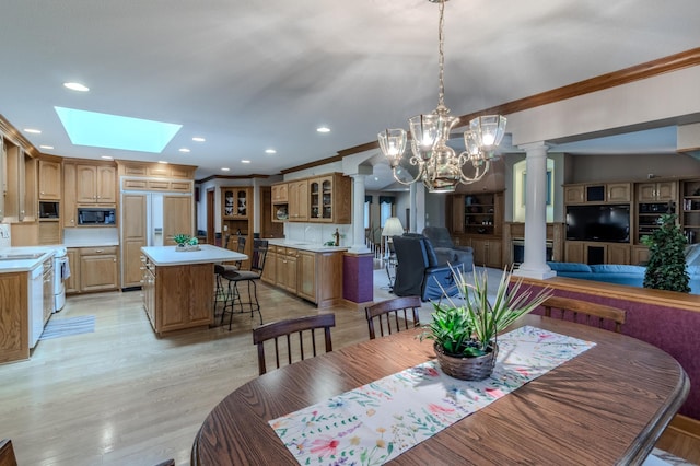 dining space with an inviting chandelier, crown molding, a skylight, light wood-type flooring, and decorative columns