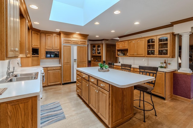 kitchen with a skylight, sink, built in appliances, a breakfast bar area, and a kitchen island