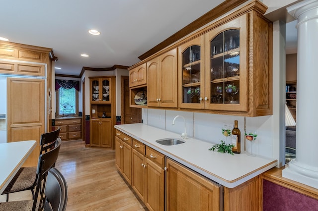 kitchen with crown molding, sink, light wood-type flooring, ornate columns, and a breakfast bar area