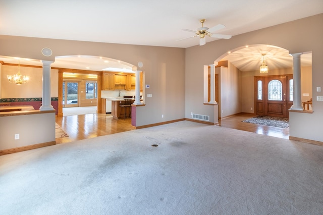 unfurnished living room with ceiling fan with notable chandelier, light colored carpet, and a wealth of natural light