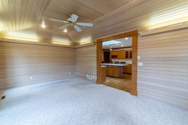 unfurnished living room with vaulted ceiling, ceiling fan, wood walls, and wood ceiling