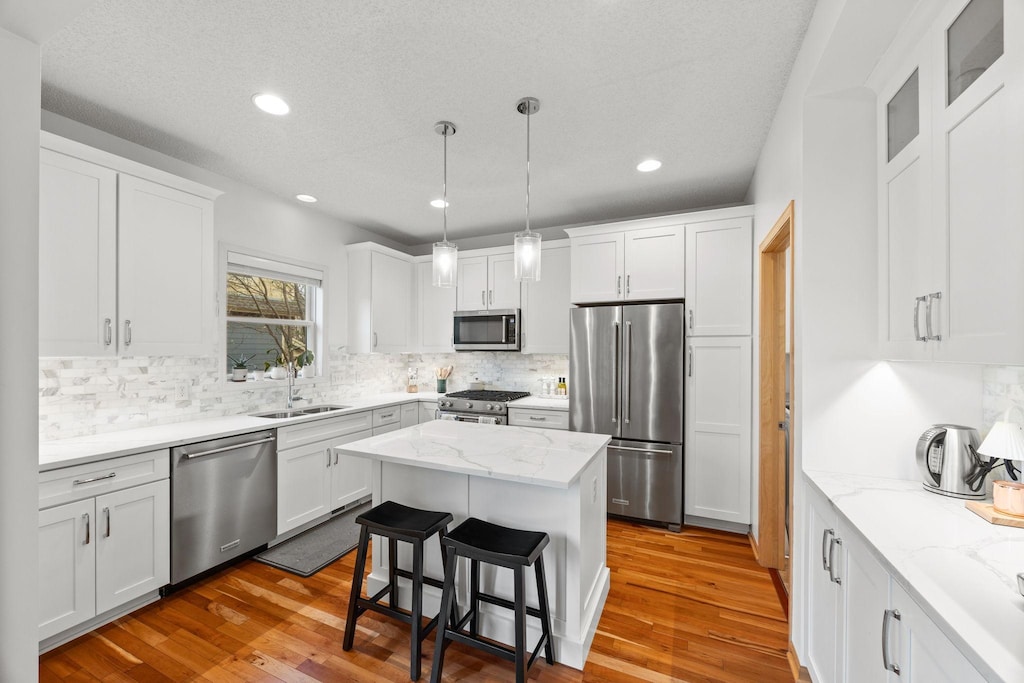 kitchen featuring a center island, high end appliances, white cabinets, sink, and light wood-type flooring