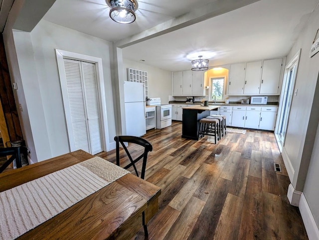 kitchen with white appliances, dark wood-type flooring, sink, a kitchen island, and white cabinetry