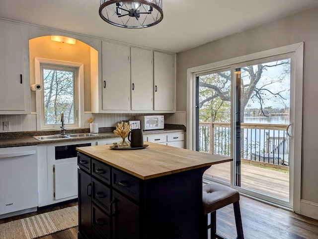 kitchen featuring white dishwasher, a center island, a water view, and white cabinetry