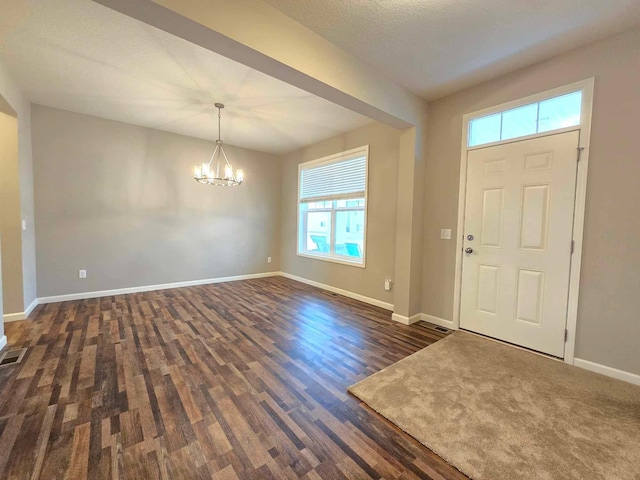 foyer with a textured ceiling, dark wood-type flooring, a wealth of natural light, and a chandelier