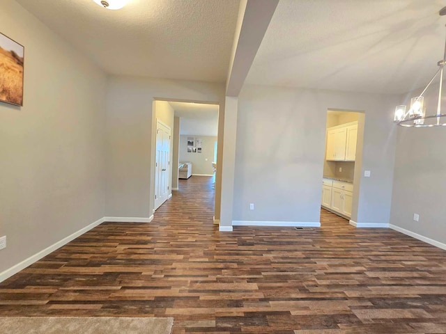 empty room with a chandelier, a textured ceiling, and dark hardwood / wood-style flooring