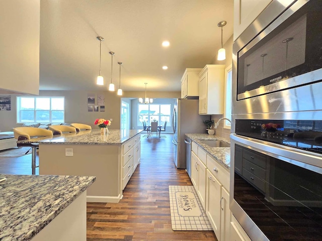 kitchen with white cabinetry, sink, hanging light fixtures, stainless steel appliances, and a kitchen island