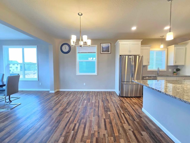 kitchen with stainless steel fridge, light stone counters, pendant lighting, dark hardwood / wood-style floors, and white cabinetry