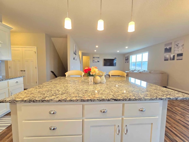 kitchen with decorative light fixtures, a center island, light stone countertops, and white cabinetry