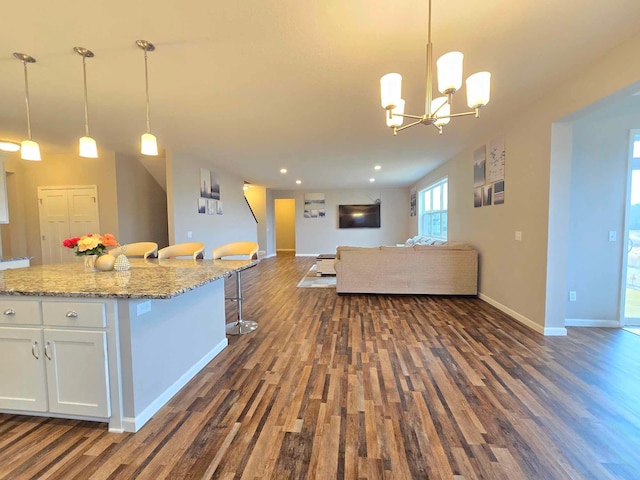 kitchen with white cabinetry, light stone countertops, dark wood-type flooring, a kitchen breakfast bar, and decorative light fixtures