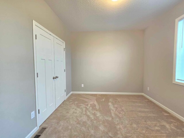 unfurnished bedroom featuring multiple windows, a textured ceiling, light colored carpet, and a closet