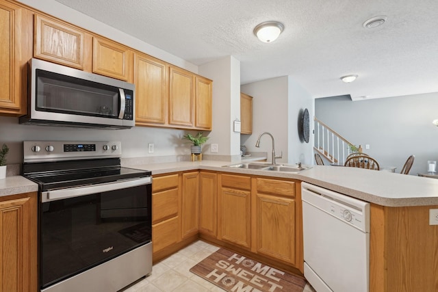 kitchen with a textured ceiling, appliances with stainless steel finishes, kitchen peninsula, and sink