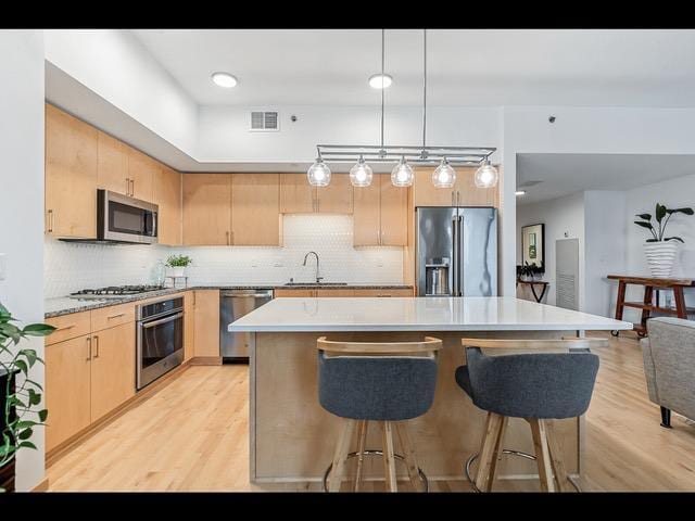 kitchen with stainless steel appliances, sink, pendant lighting, light brown cabinets, and a kitchen island