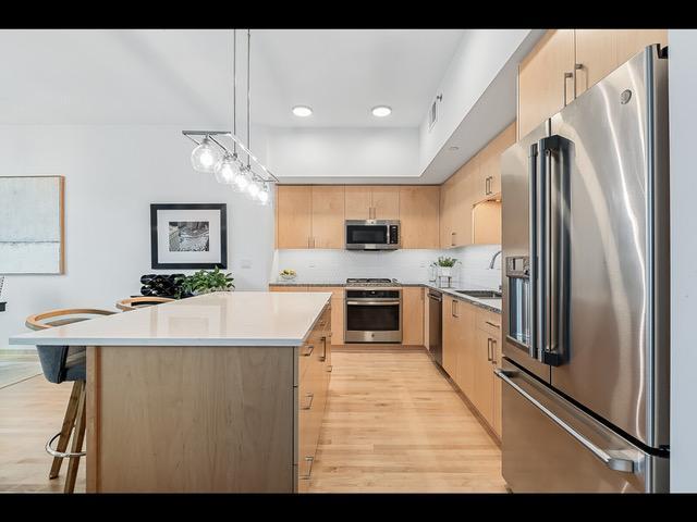 kitchen featuring light brown cabinets, a center island, backsplash, decorative light fixtures, and appliances with stainless steel finishes