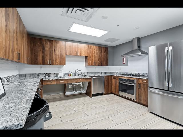 kitchen featuring light stone countertops, appliances with stainless steel finishes, backsplash, wall chimney exhaust hood, and sink