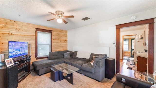 205 Broadway St SE, Isanti, MN 55040 - living room featuring wooden walls, ceiling fan, plenty of natural light, light colored carpet, and a textured ceiling