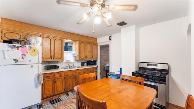 205 Broadway St SE, Isanti, MN 55040 - kitchen featuring freestanding refrigerator, stainless steel range with gas stovetop, ceiling fan, light countertops, and brown cabinets