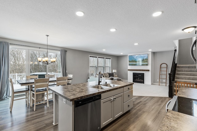 kitchen with a large fireplace, dishwasher, sink, an island with sink, and pendant lighting