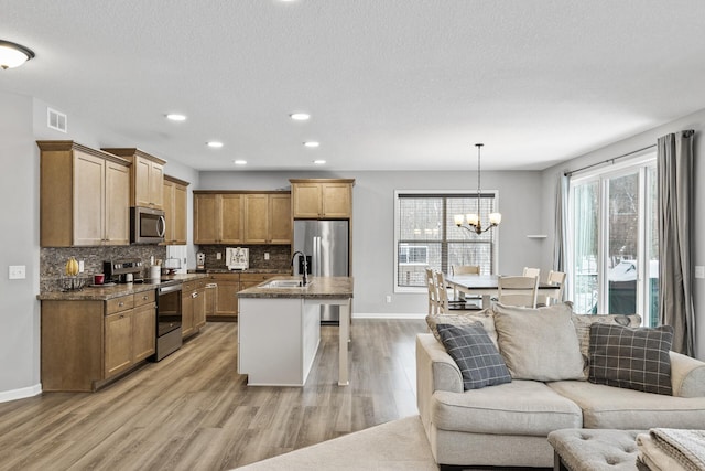 kitchen featuring light wood-type flooring, stainless steel appliances, sink, decorative light fixtures, and an inviting chandelier