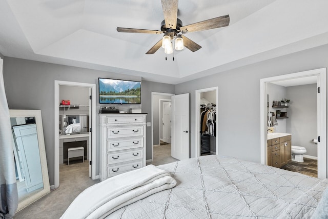 carpeted bedroom featuring ceiling fan, a walk in closet, ensuite bathroom, and a tray ceiling