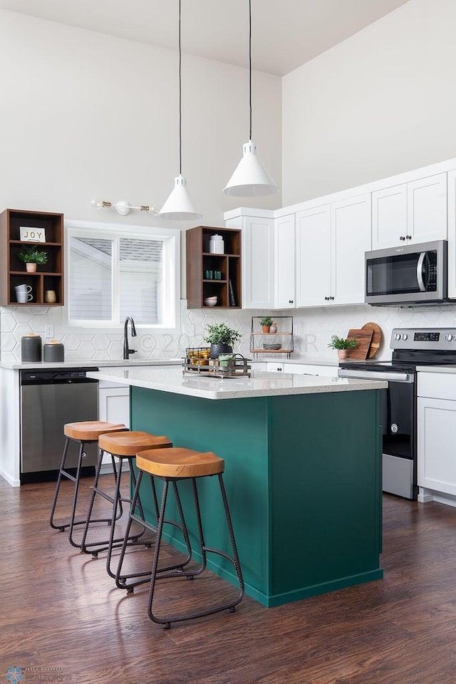 kitchen with a center island, white cabinets, dark hardwood / wood-style floors, decorative light fixtures, and stainless steel appliances