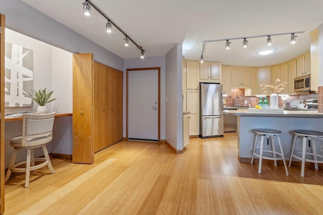 kitchen with decorative backsplash, appliances with stainless steel finishes, a breakfast bar area, light wood-style floors, and a sink