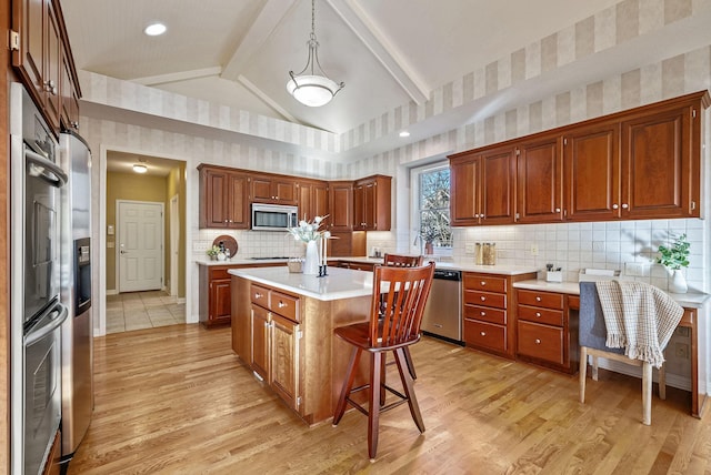 kitchen with decorative light fixtures, a kitchen island, stainless steel appliances, and light hardwood / wood-style flooring