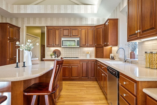 kitchen with backsplash, sink, appliances with stainless steel finishes, light hardwood / wood-style floors, and a breakfast bar area