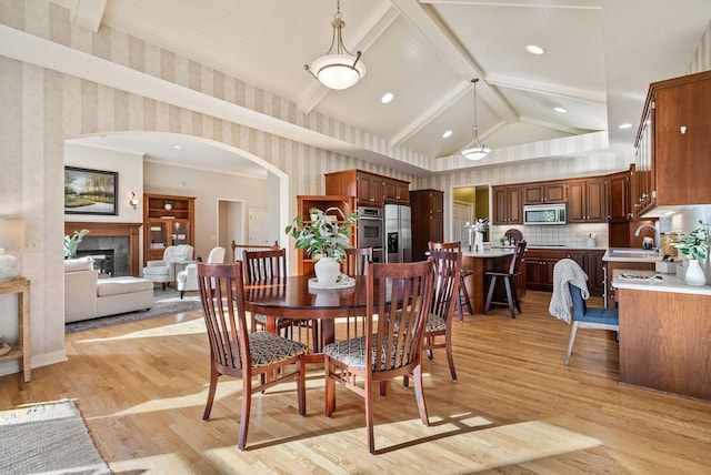 dining room featuring a tile fireplace, lofted ceiling with beams, and light hardwood / wood-style floors